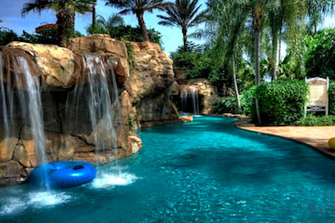 Mid shot of a lazy river with tall brown rocks and waterfalls on the left and palm trees in the distance.