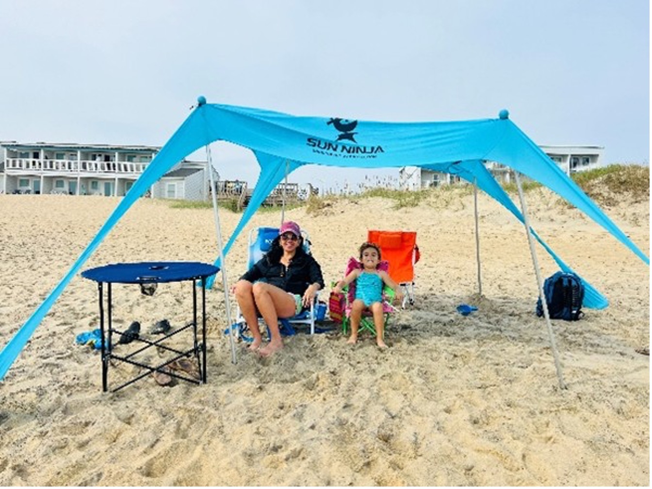 Mother and daughter enjoying themselves seated on the beach under a canopy