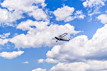 Long shot with small plane airborne among fluffy white clouds and blue skies