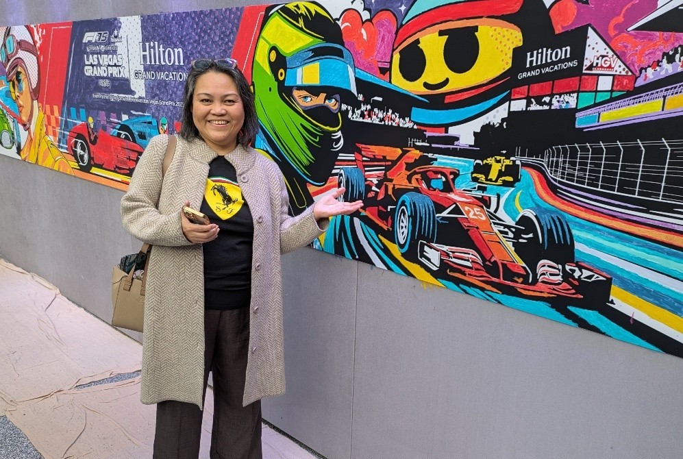 Smiling woman standing in front of a colorful Hilton Grand Vacations F1 mural