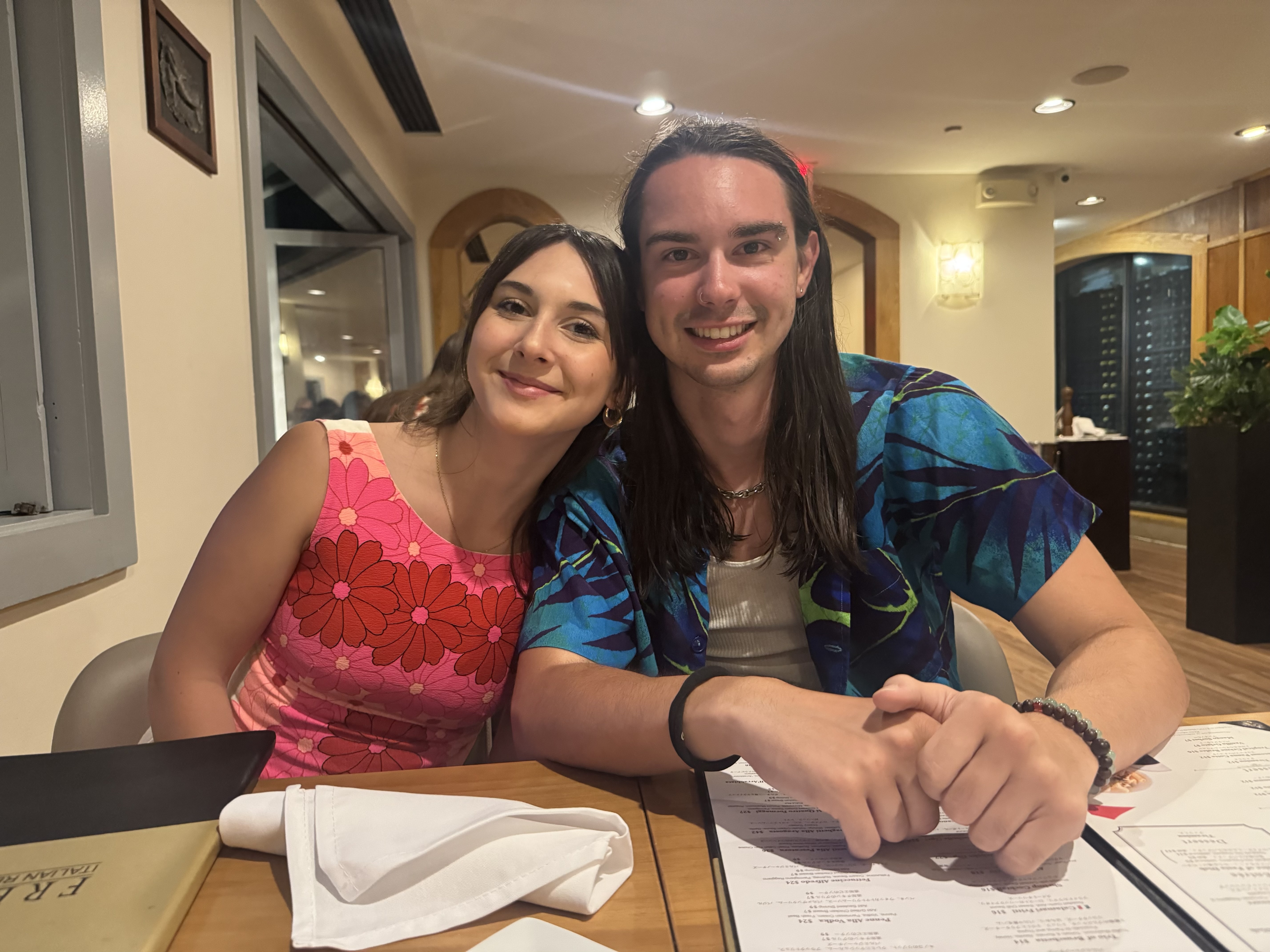 Two family members in colorful clothing, smiling, sitting in a restaurant with menus.