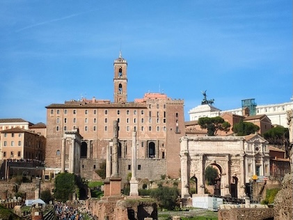 Picture of the Roman Forum surrounded by ruins of ancient buildings and columns in the foreground and a brilliant blue sky in the background.