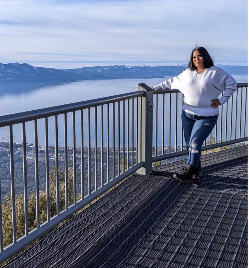 Woman standing on a tiled deck with a railing overlooking Lake Tahoe and mountains in the background