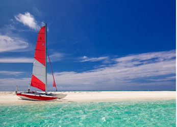 A red and white striped catamaran sits on a pristine and empty white sand beach under deep blue skies and sparkling turquoise water.