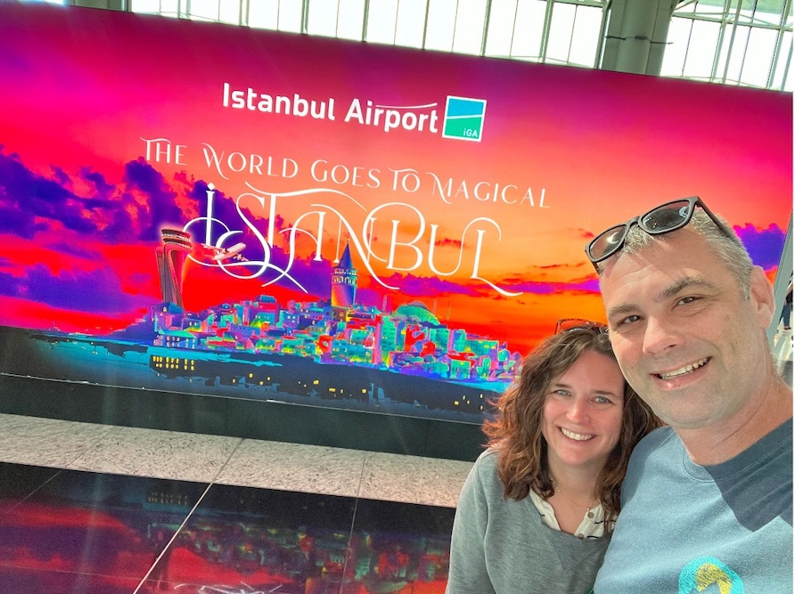 Couple posing and smiling in front of a welcome to Istanbul airport sign.