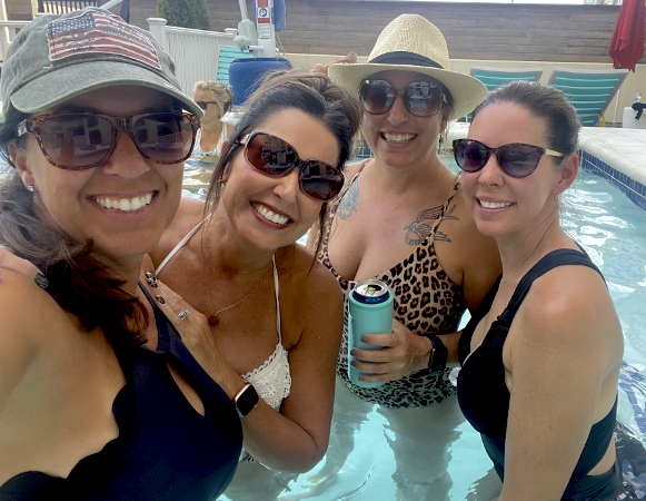 Four smiling ladies with sunglasses posing in a pool