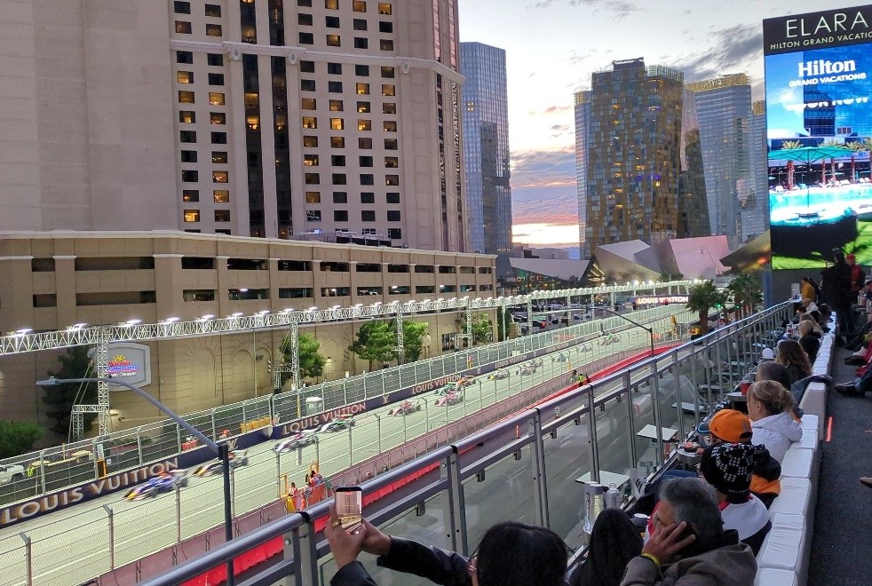Fans sitting in the stands cheering as race cars go by on a track