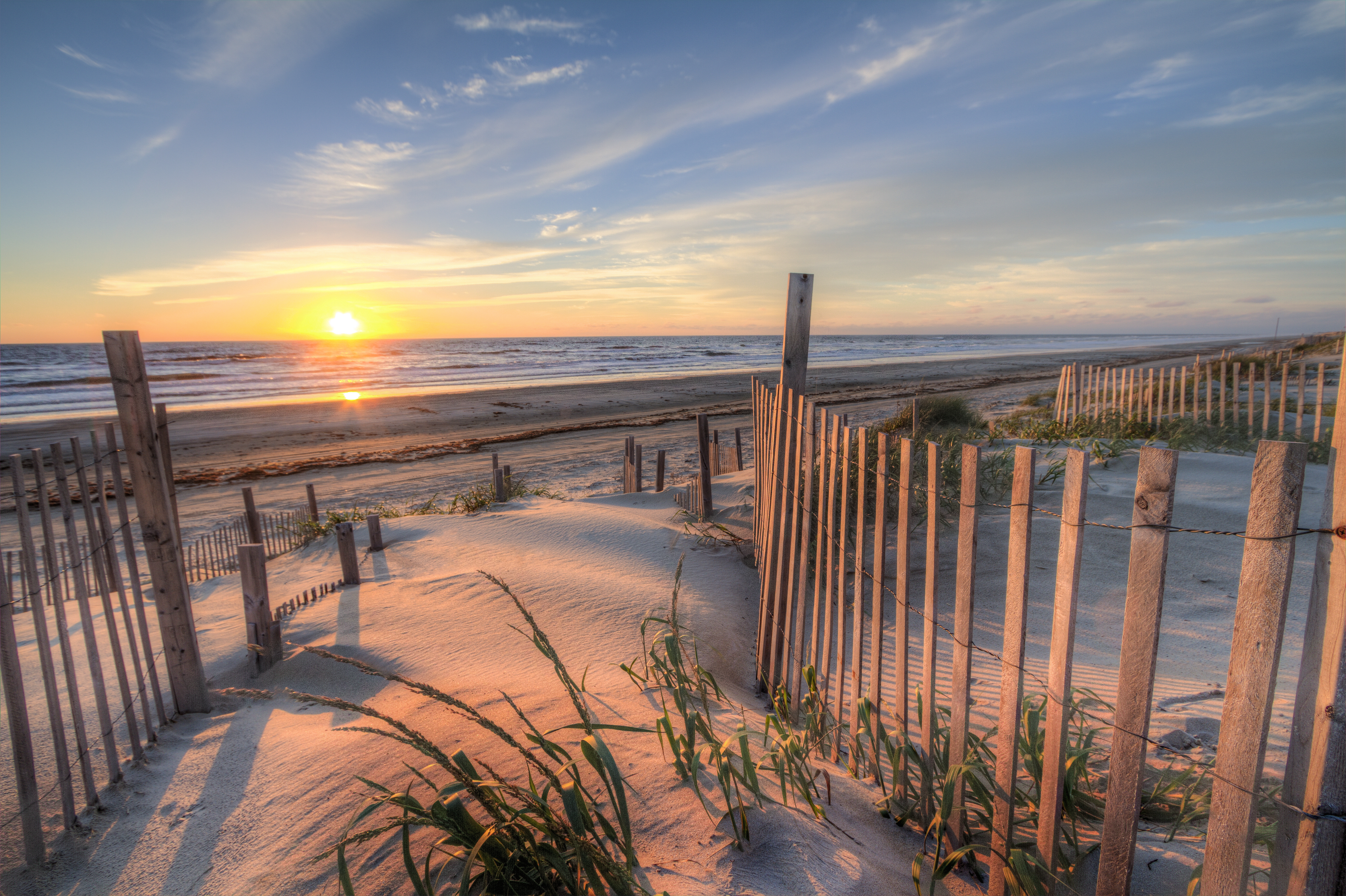 Stunning beach scene of a winding path in the sand, blue ocean in the background and golden sunset on the horizon