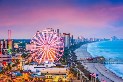 Drone view of the Myrtle Beach shoreline and boardwalk at sunset under pink and blue skies.
