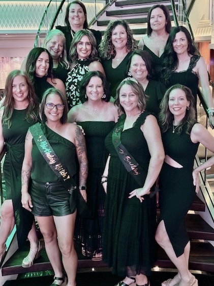 Group of 13 female friends in black with Happy Birthday banners pose on cruise ship steps.