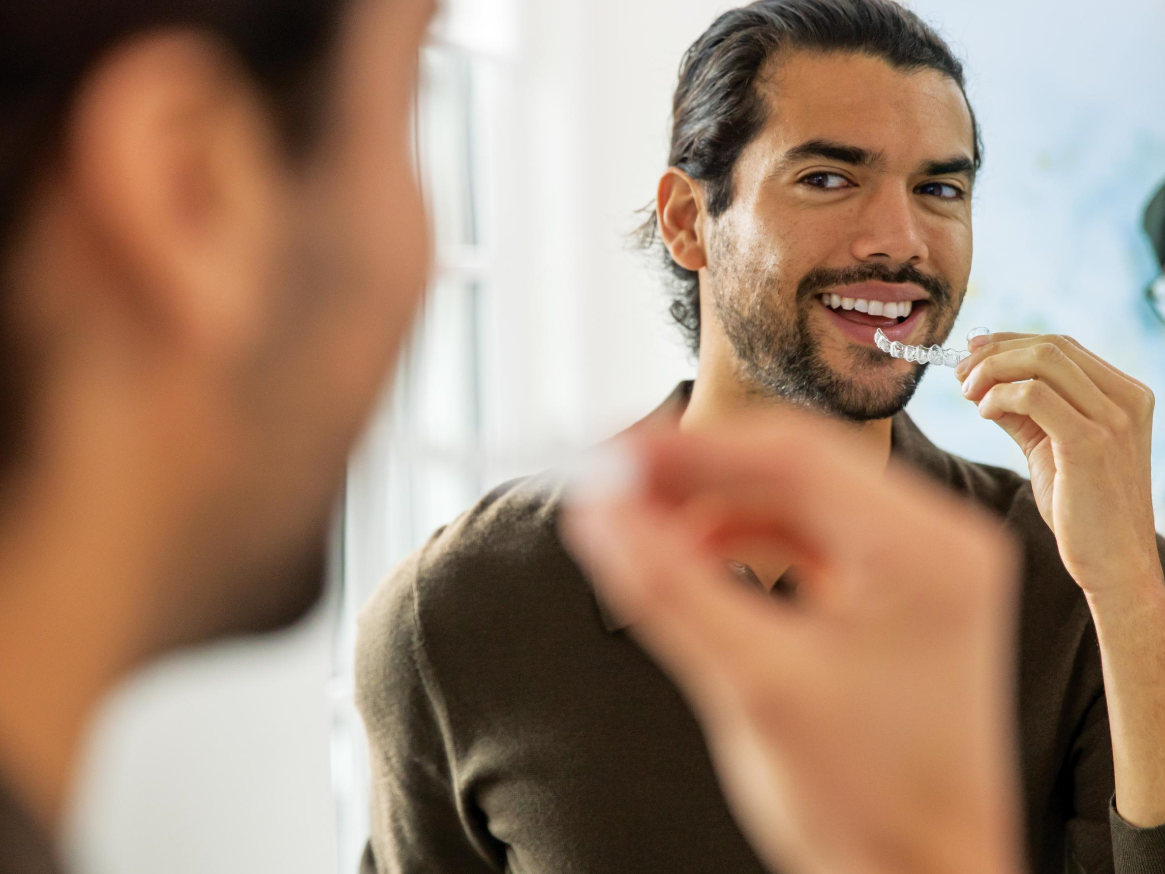 Young man smiling to the mirror while putting in his aligners