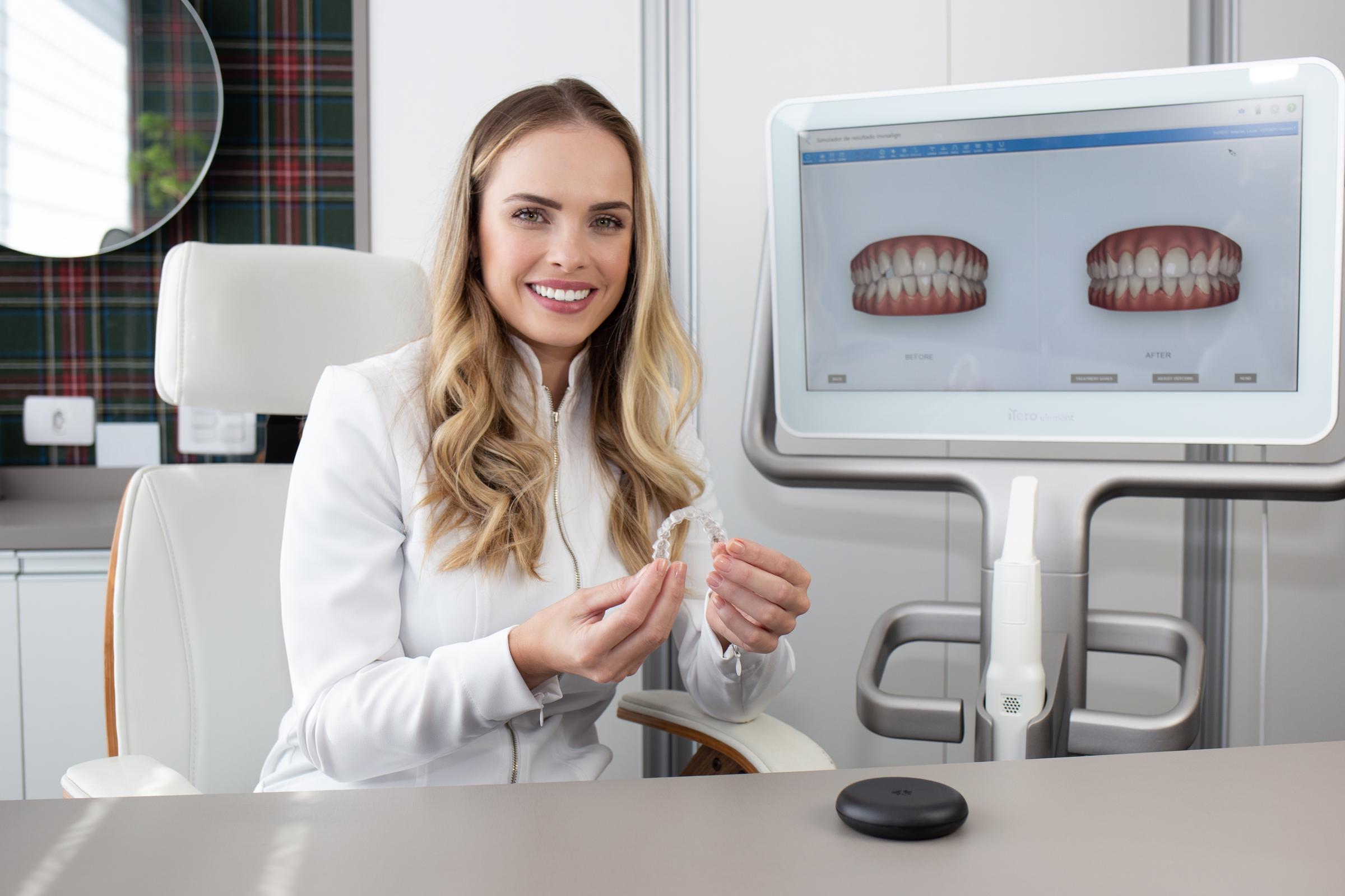 Blonde Invisalign female doctor smiling to the camera while holding clear aligners