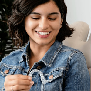 Young woman smiling and holding her Invisalign® clear aligners