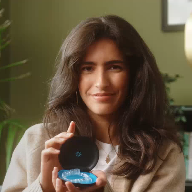 امرأة شابة تبتسم وتعرض تقويم Invisalign® الشفاف في علبته
