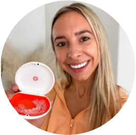 Kobieta uśmiecha się i pokazuje swoje nakładki Invisalign® w etui