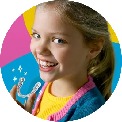 Una bambina che sorride e tiene in mano gli aligner Invisalign® su uno sfondo colorato