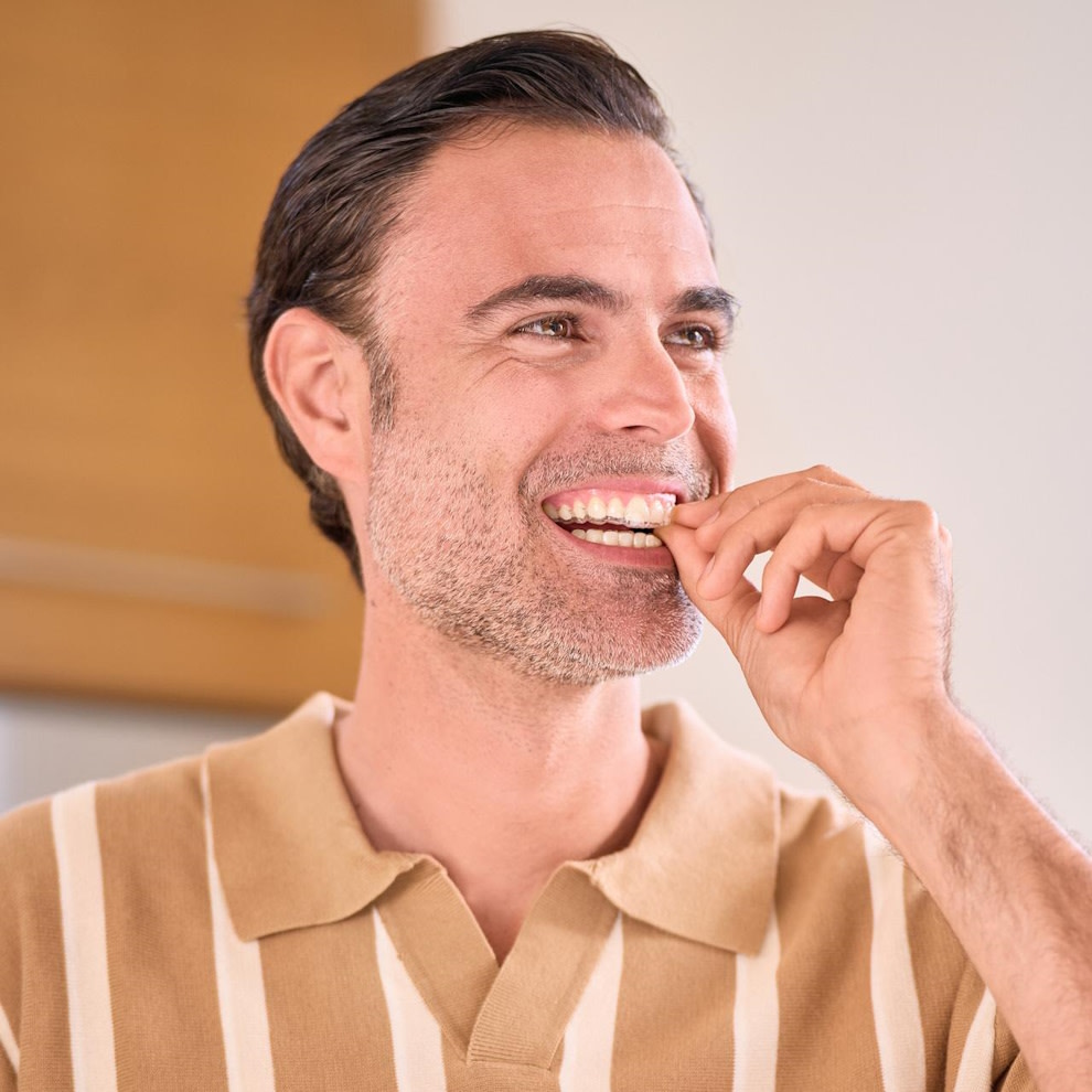 Un uomo con una camicia a righe indossa gli allineatori Invisalign®