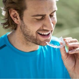 Bir erkek Invisalign® şeffaf plaklarını tutuyor ve gülümsüyor