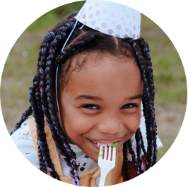 فتاة صغيرة ترتدي قبعة حفلة وتأكل الكعكة
