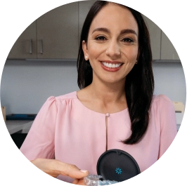 Una donna con una camicia rosa tiene in mano gli aligner Invisalign® e sorride