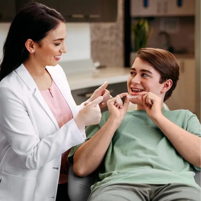 Female doctor explaining how to wear Invisalign® aligners to a smiling teenage patient