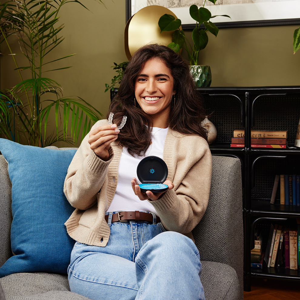 Genç bir kadın gülümsüyor ve Invisalign® şeffaf plaklarını kutusunda gösteriyor