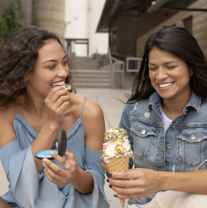 Two young women are eating ice cream and one of them puts the Invisalign® aligners in their case