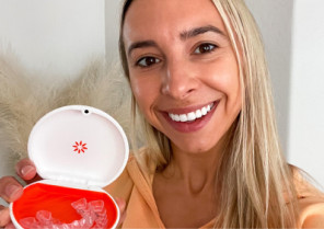 Blonde woman smiling and showing her Vivera retainers inside an orange and white case