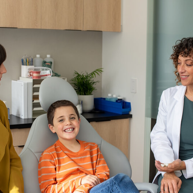 Lekarz wyjaśnia leczenie Invisalign® uśmiechniętemu chłopcu i jego mamie podczas konsultacji
