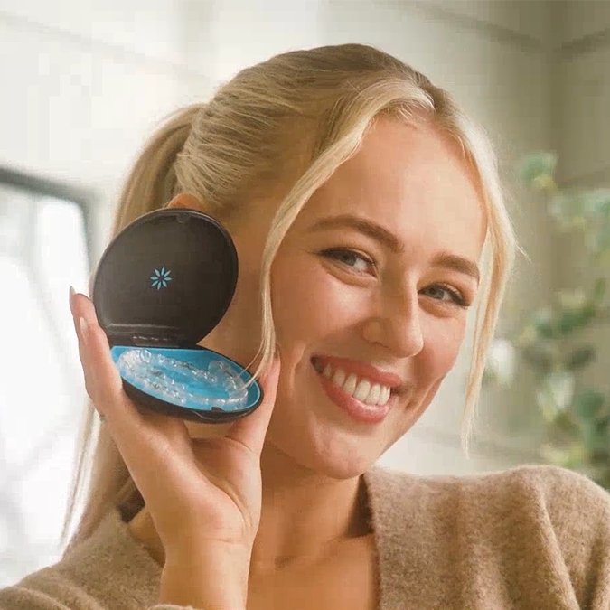 فتاة تبتسم وتعرض تقويم Invisalign® الشفاف في علبته
