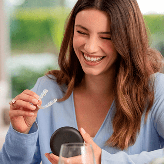 Ragazza con maglione blu che sorride e tiene in mano gli aligner Invisalign®
