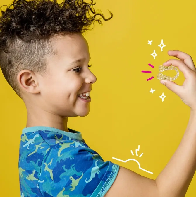 Un ragazzo che tiene in mano gli aligner Invisalign® First su uno sfondo giallo