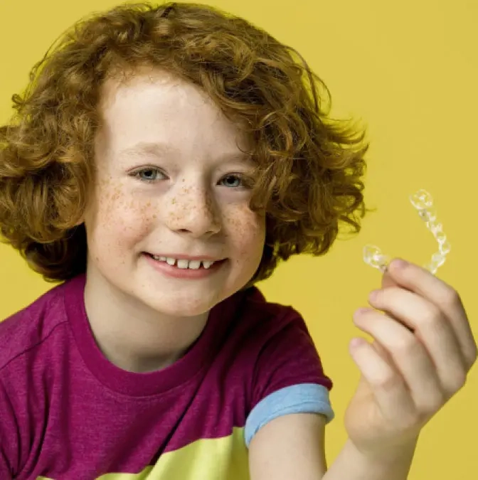 Happy kid with his new Invisalign® aligner on yellow background