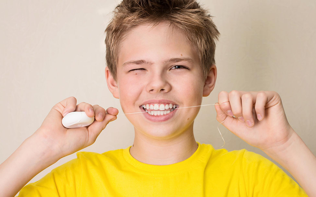 Un bambino che usa il filo interdentale con una maglietta gialla