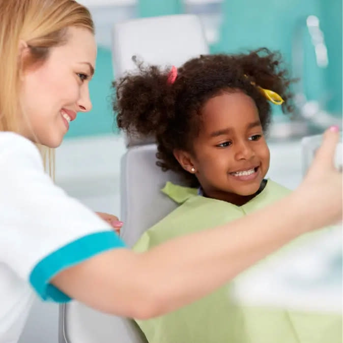 Female doctor shows little girl her teeth after Invisalign® treatment