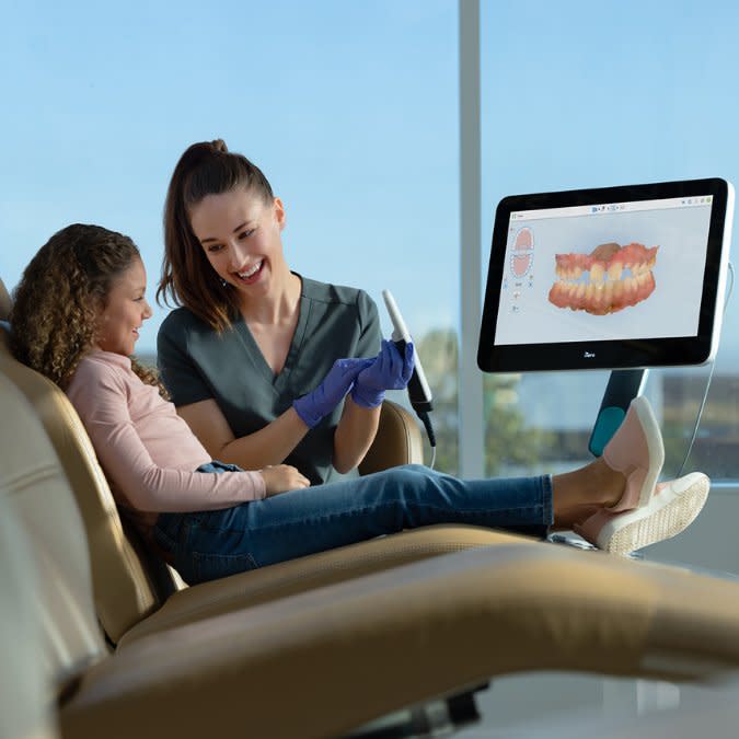 Kadın doktor, küçük kıza Invisalign® tedavisinden sonra dişlerini gösteriyor
