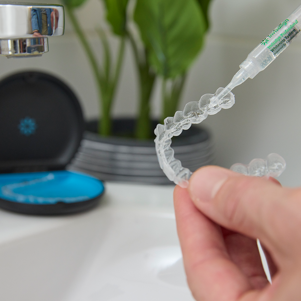Invisalign® aligners are filled with whitening gel from a syringe on the background of a case from aligners