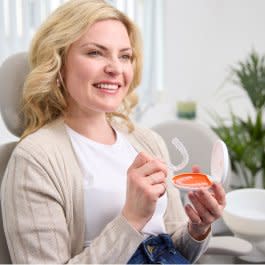 Genç bir kadın gülümsüyor ve Vivera™ pekiştirme plak kutusunu gösteriyor