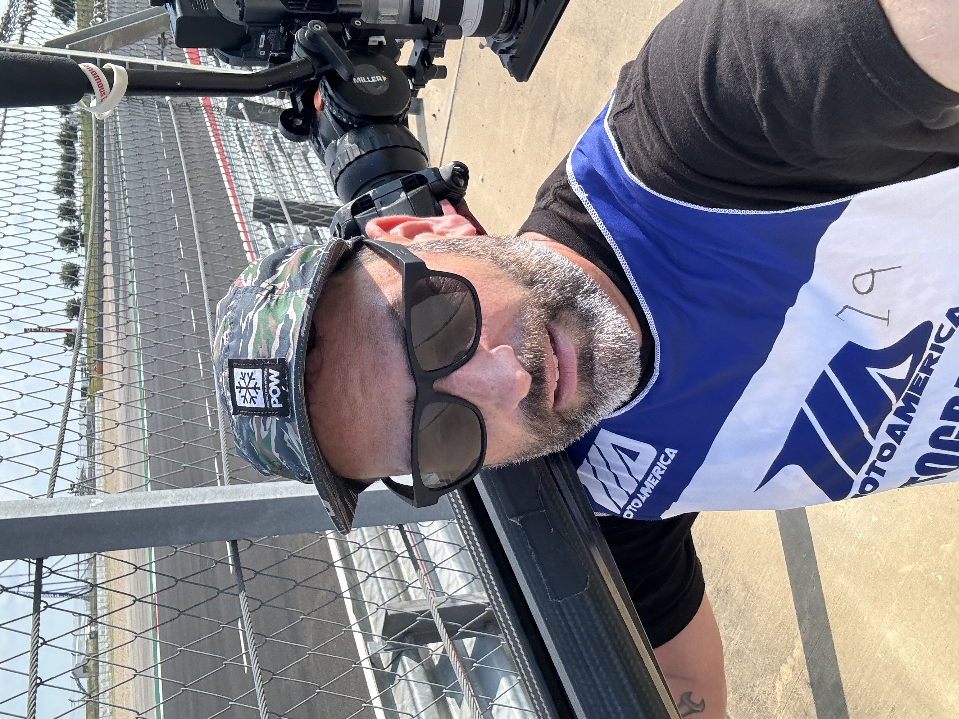 Documentary cinematographer Kyle Decker carrying a cinema camera between corners during a Harley-Davidson King of the Baggers race weekend.