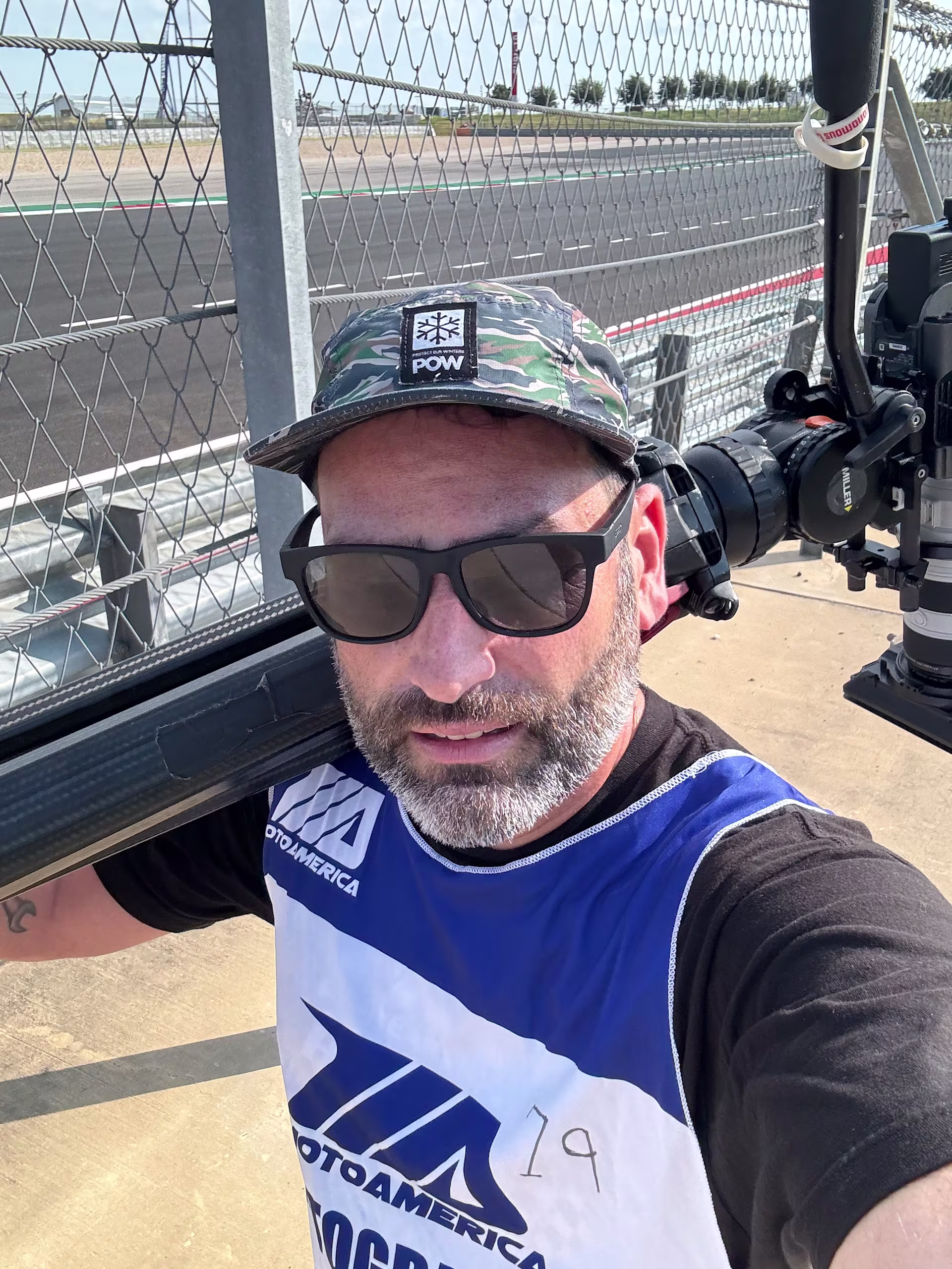Documentary cinematographer Kyle Decker carrying a cinema camera between corners during a Harley-Davidson King of the Baggers race weekend.
