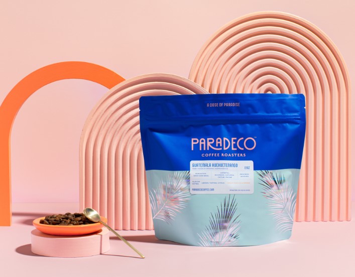 Bolsa de café azul con hojas de palma holográficas brillantes sobre fondo rosa con taza de café rosa