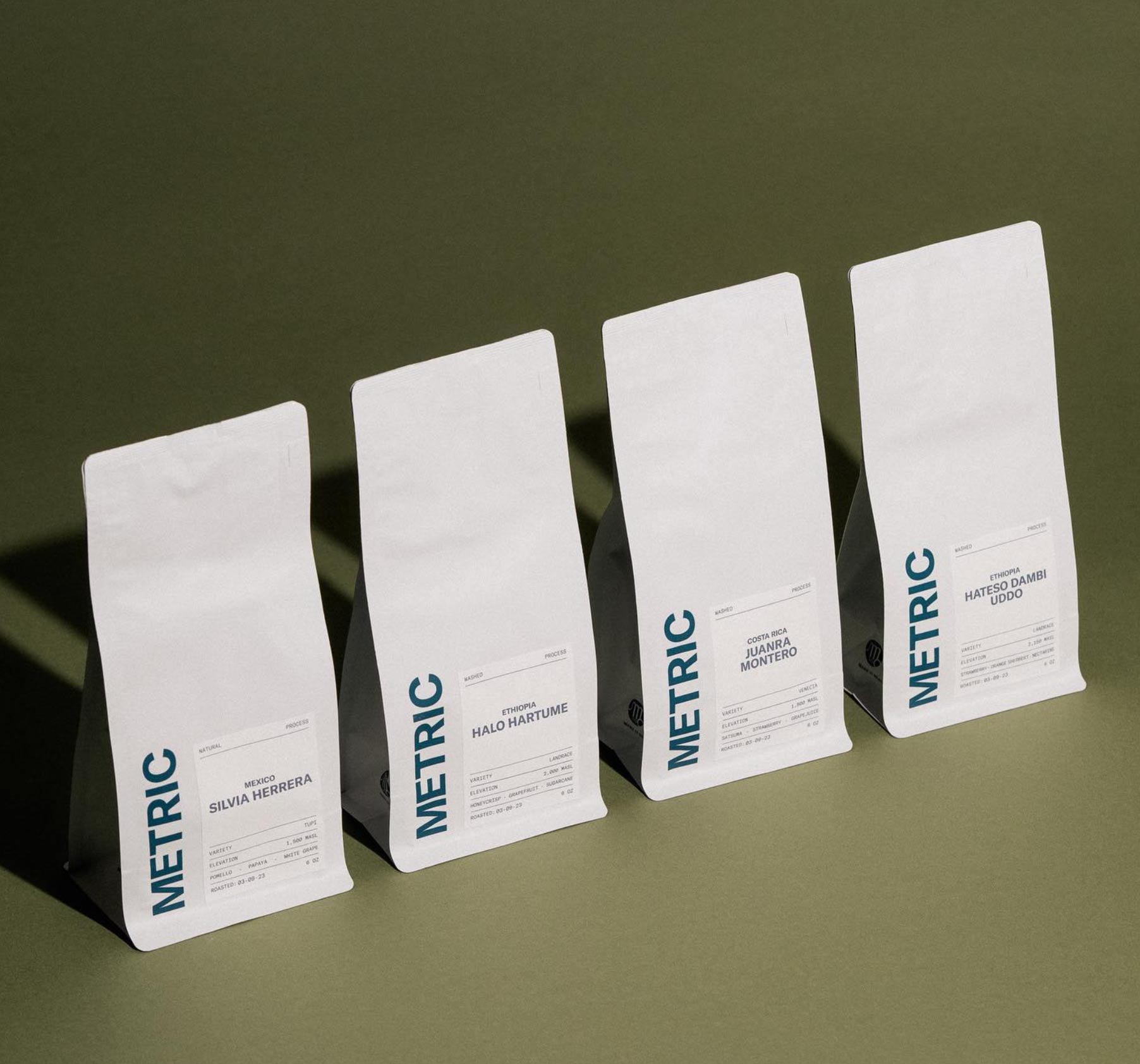 Four Metric Coffee bags in minimalist white packaging with bold blue branding, designed by Savor Brands, showcasing modern and sustainable coffee packaging innovation