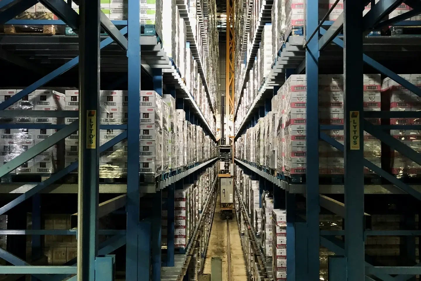 Tall blue metal shelving units filled with stacked boxes in a warehouse aisle