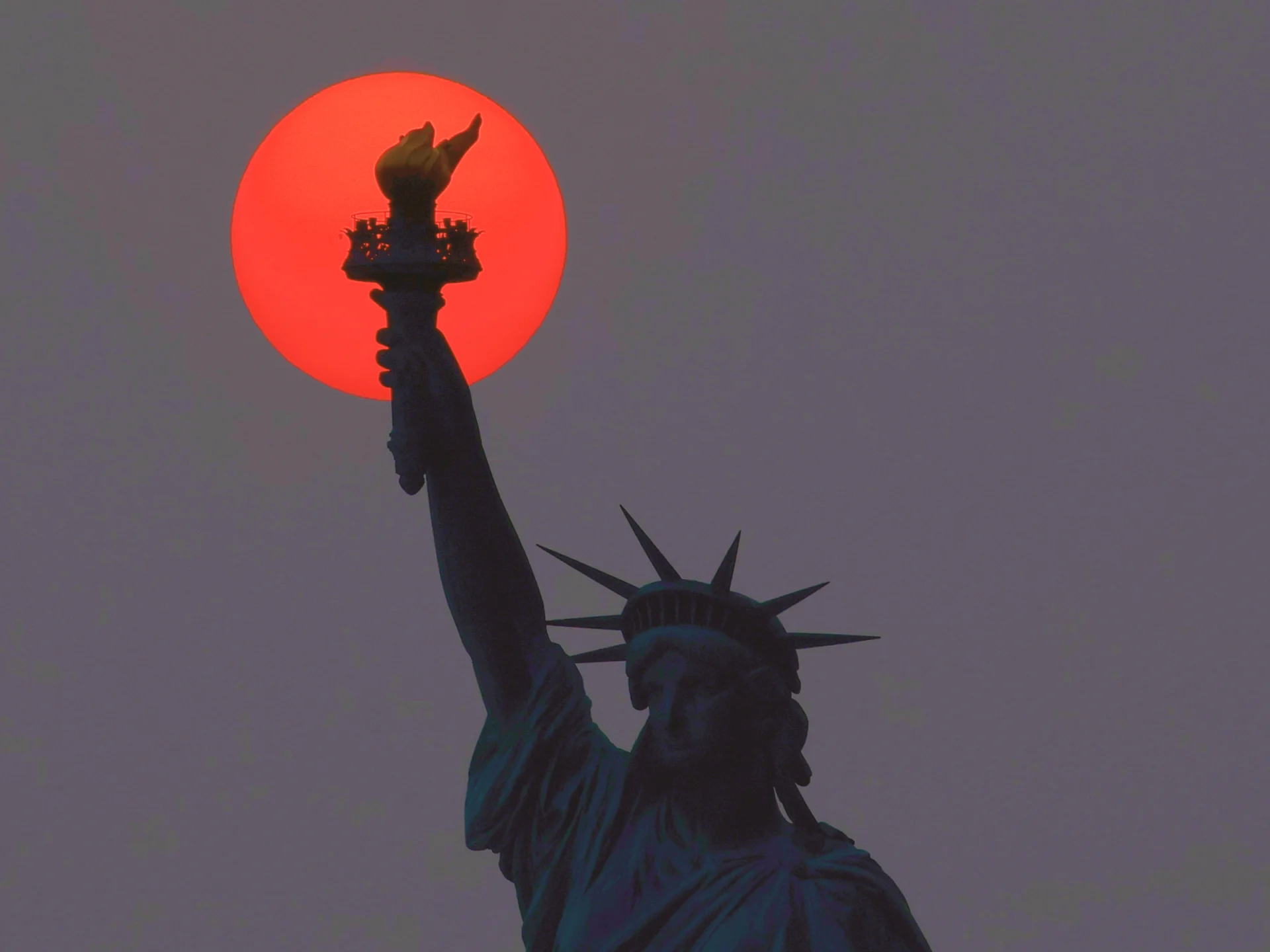 A silhouette of the Statue of Liberty is set against a red sky, highlighting its iconic form and presence.