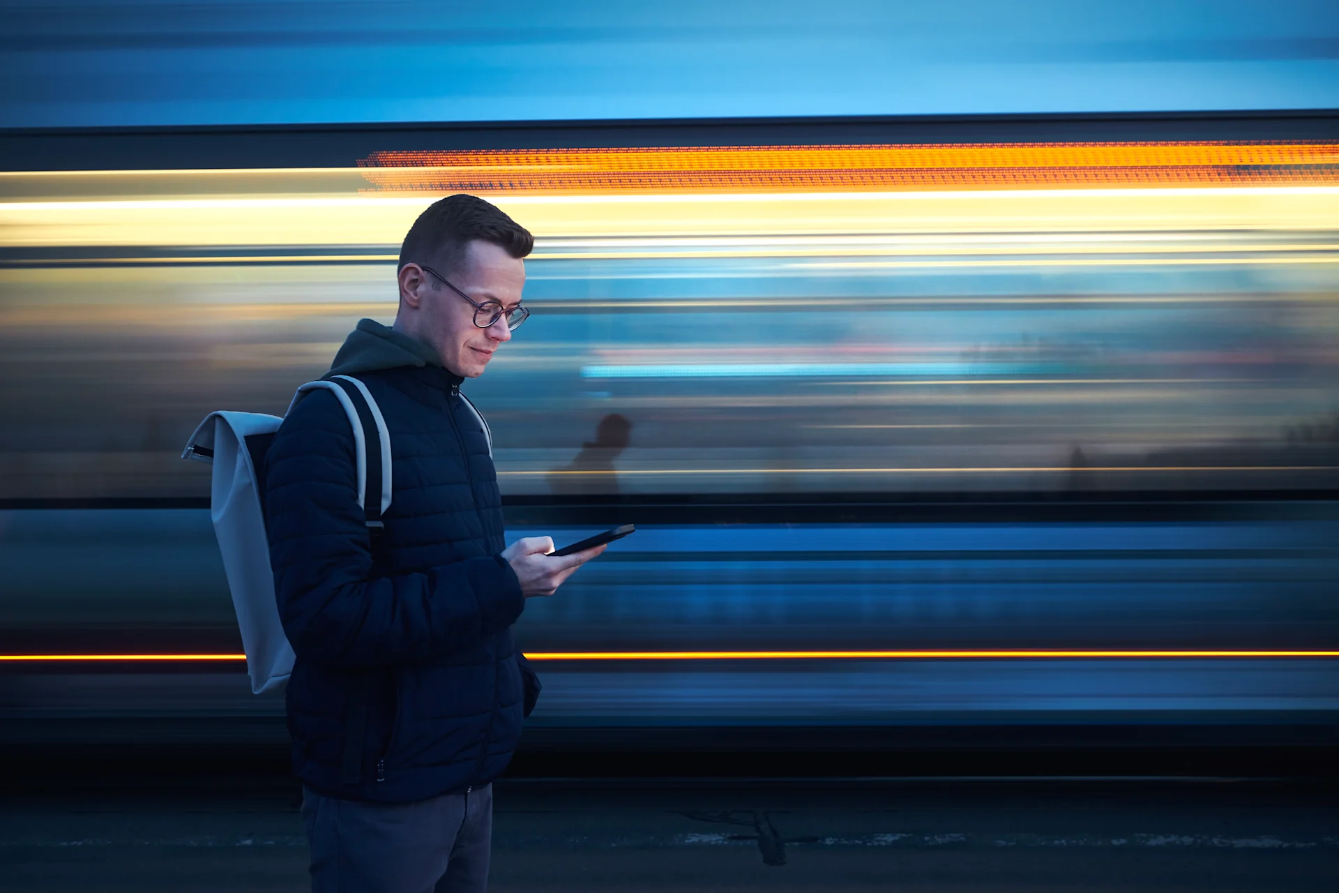 Man with backpack holding and using phone against tram in blurred motion