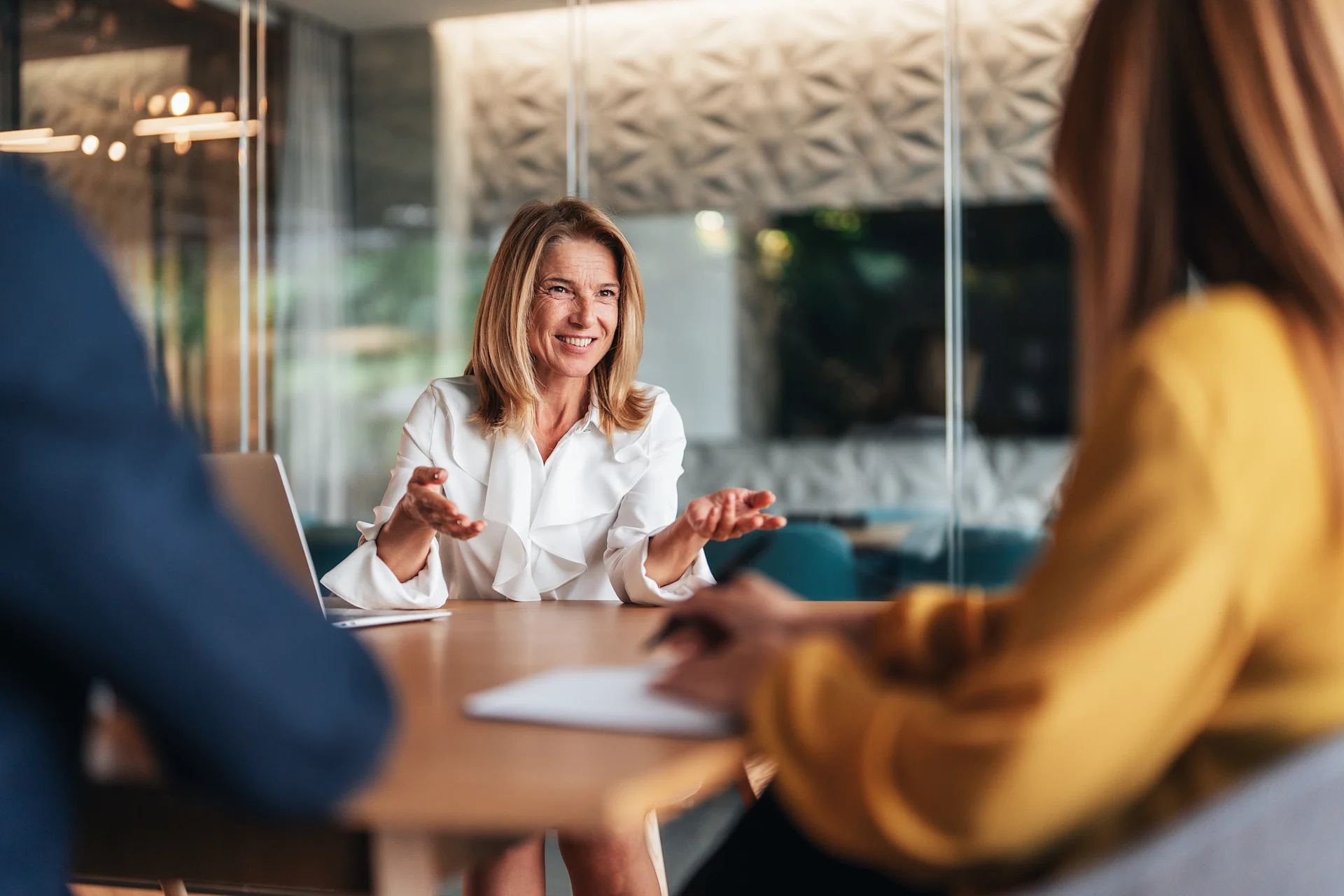 A woman speaks to other collaborators in a meeting setting, highlighting an interactive dialogue between the participants.
