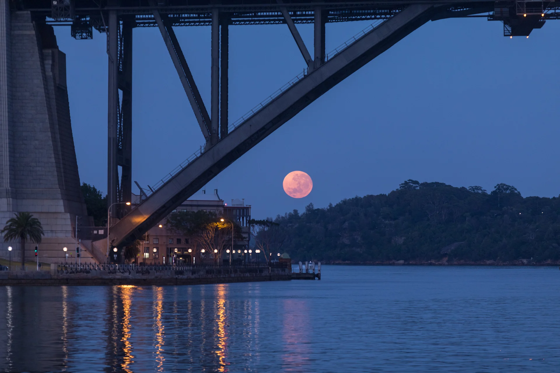 A bright full moon ascends above the water, illuminating the night sky and creating a serene atmosphere.