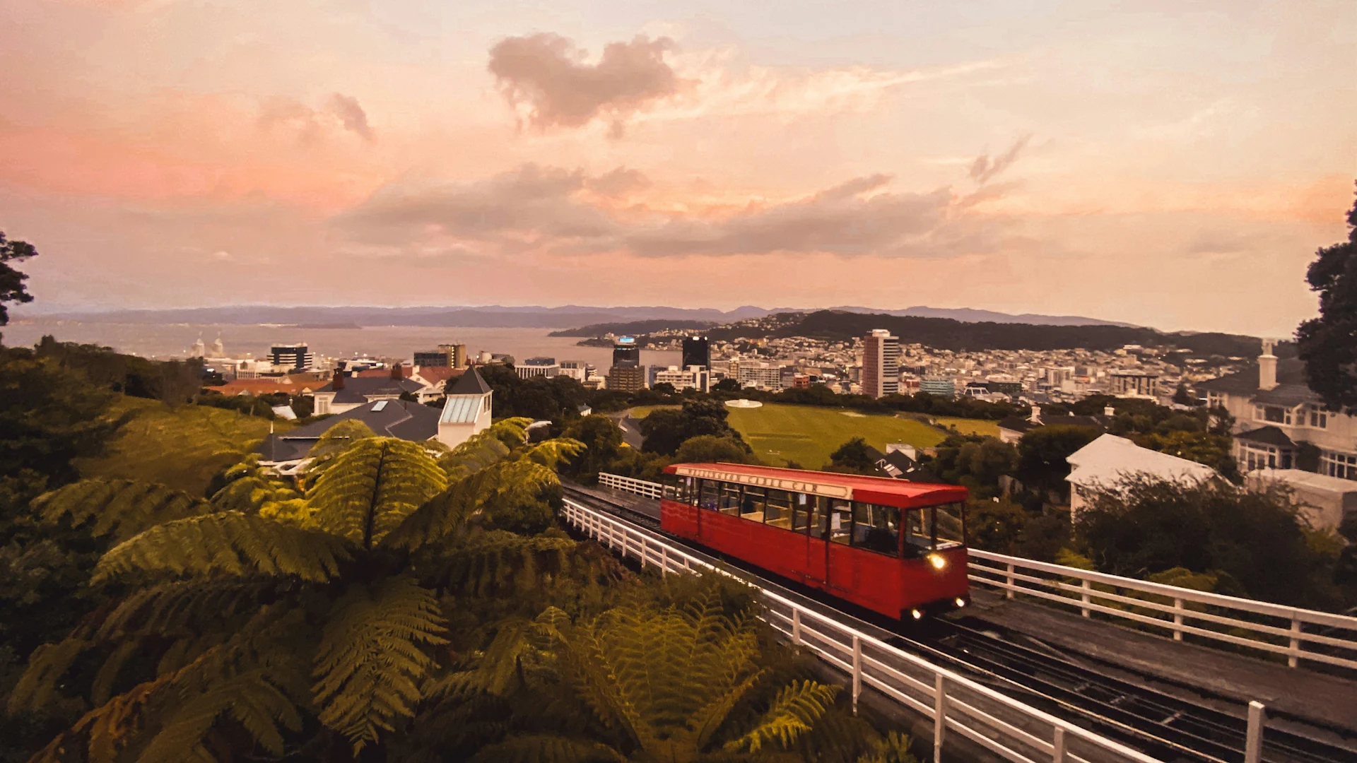 A colorful tram moves along Christchurch, New Zealand, with a city skyline visible in the background, showcasing urban transportation.