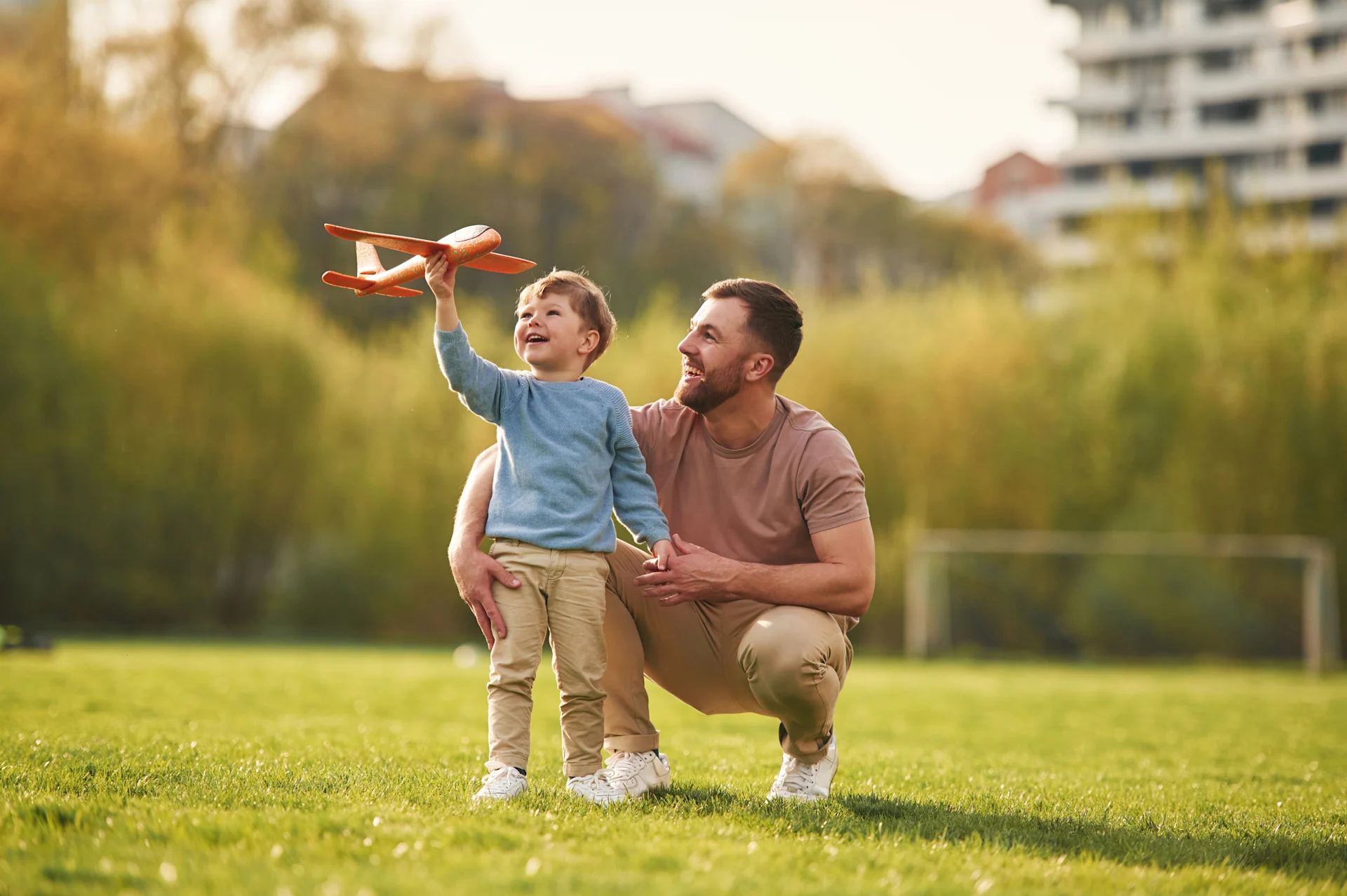 Father and son playing with a model airplane in a grass field 
