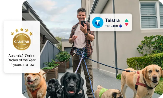 A professional dog walker with 5 dogs attached by leads to his belt is standing in a car driveway, looking at his phone. An overlay shows he's looking at Telstra shares.